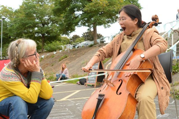 A cello lesson outside. With the tutor sitting and watching the student play