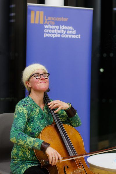 A female playing the cello and looking up in front of a blue popup banner.