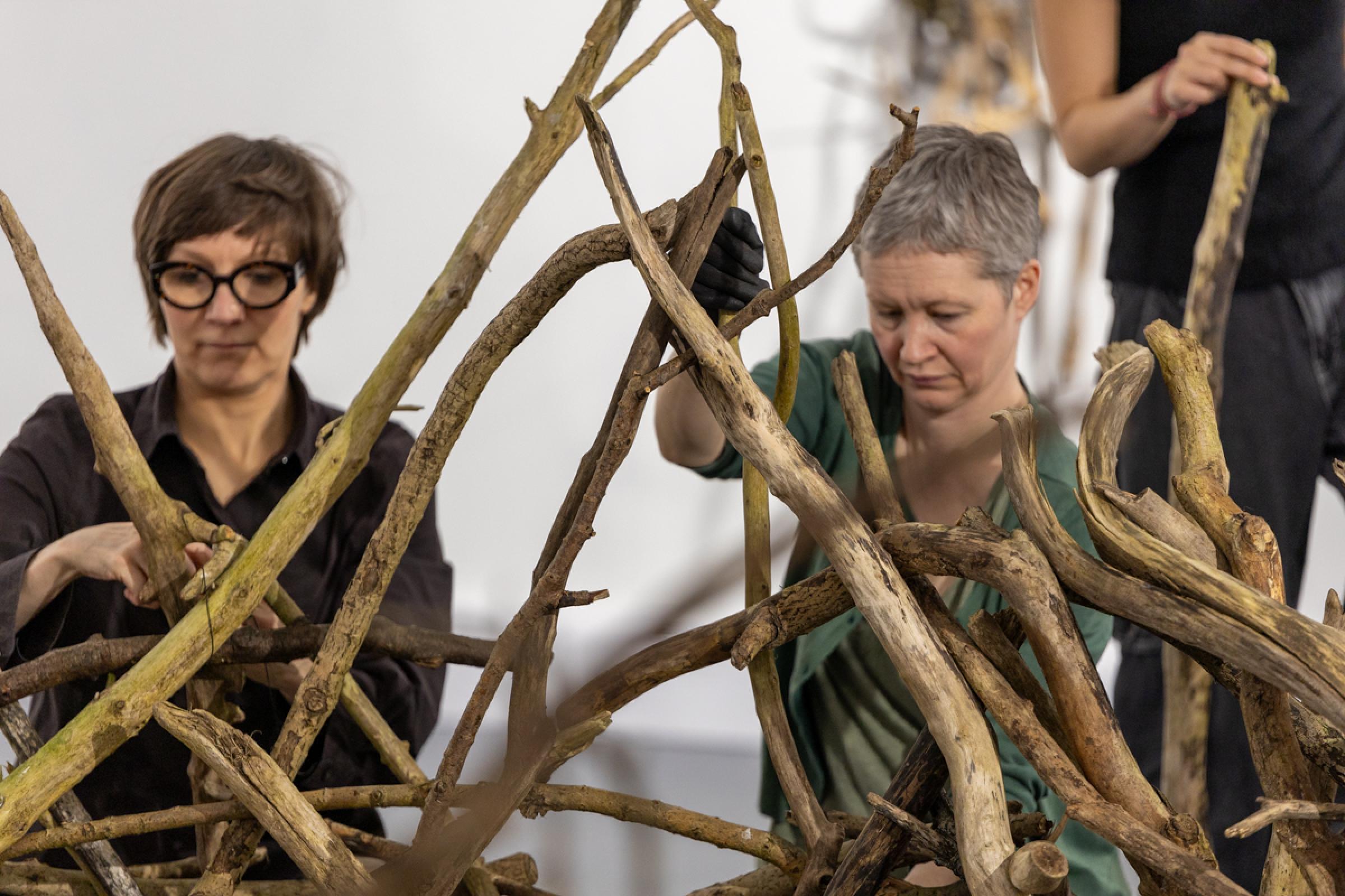 Two people building a large nest in a gallery