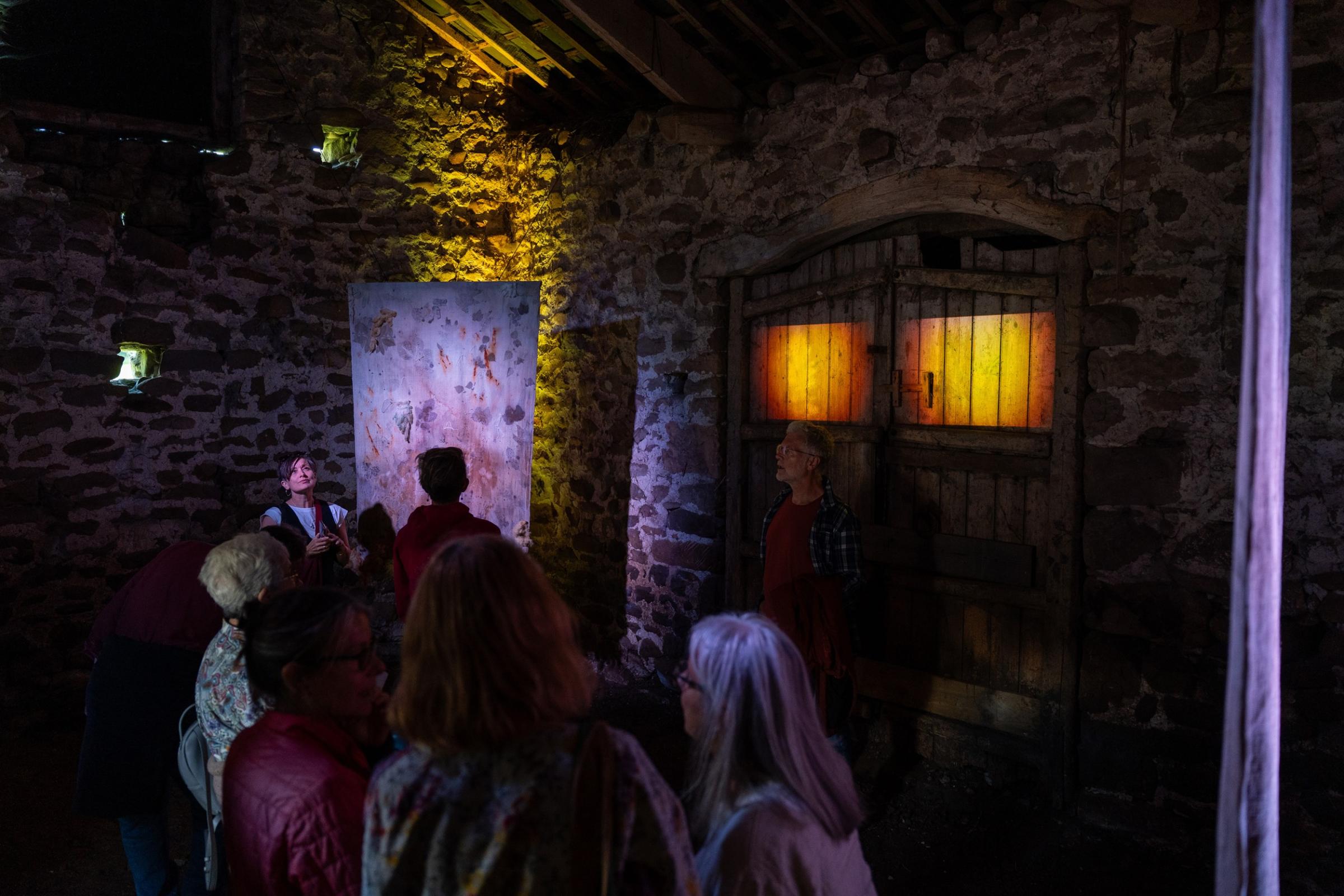 People looking at an art installation in a barn with projection and hanging textiles