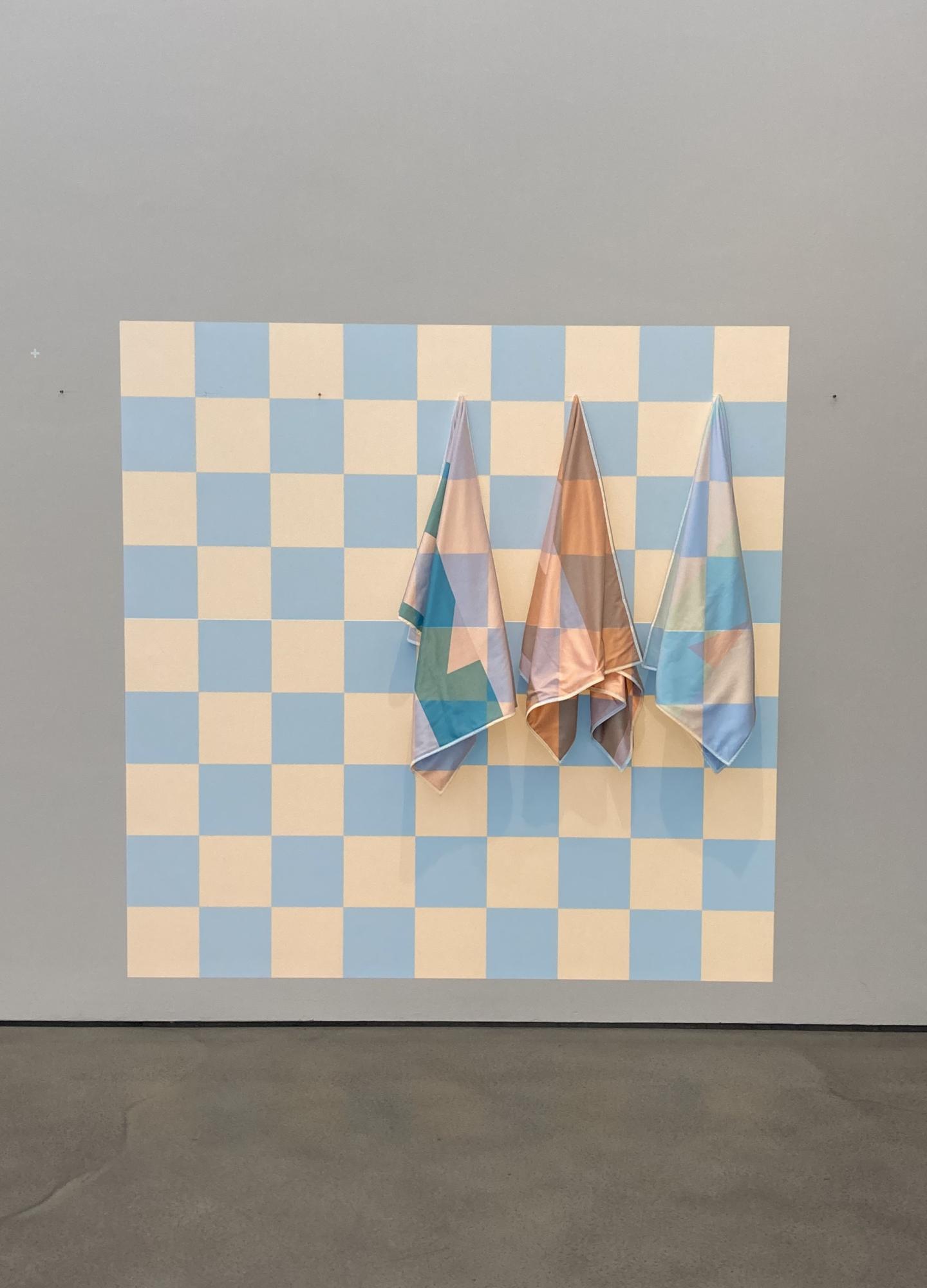 Artwork of projected checkerboard on a wall with three fabrics hanging from hooks