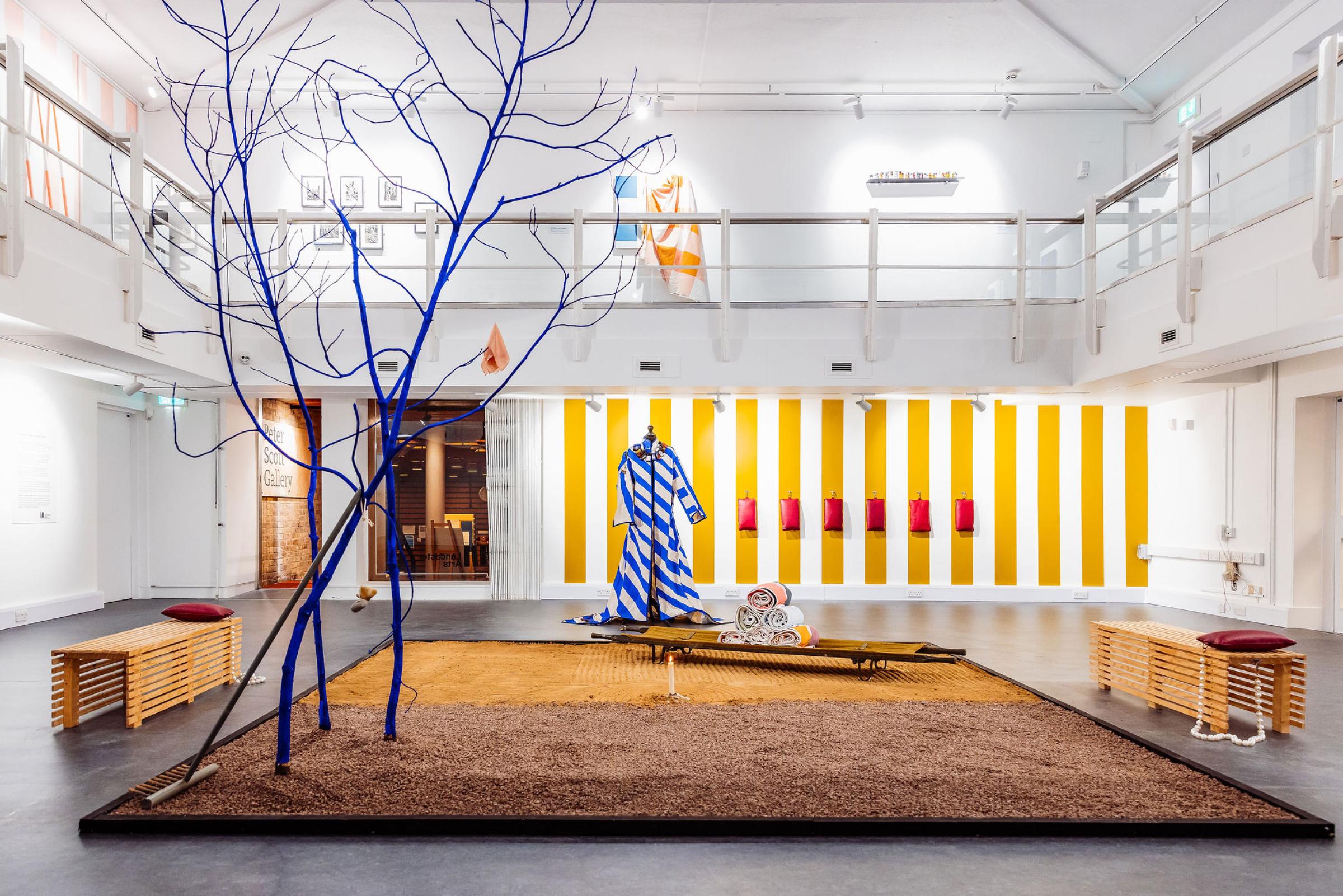 A zen garden of sand and gravel and a blue tree in an art gallery with one yellow and white striped wall
