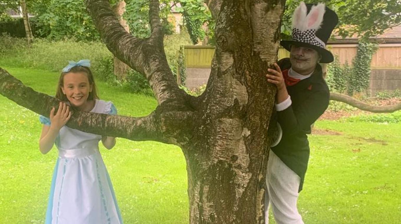 Alice in Wonderland and the 'Mad Hatter' stood outside by a tree