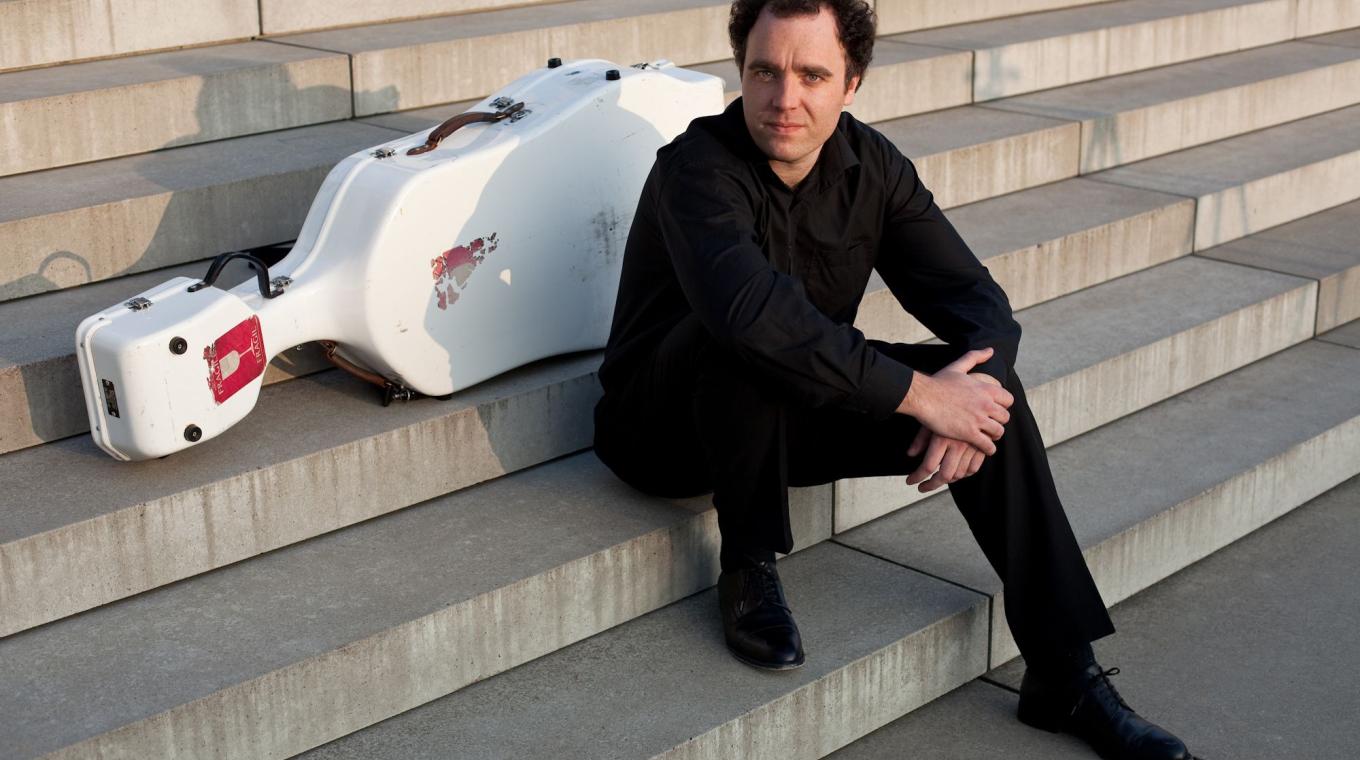 A man sat on wide steps with a cello case behind him