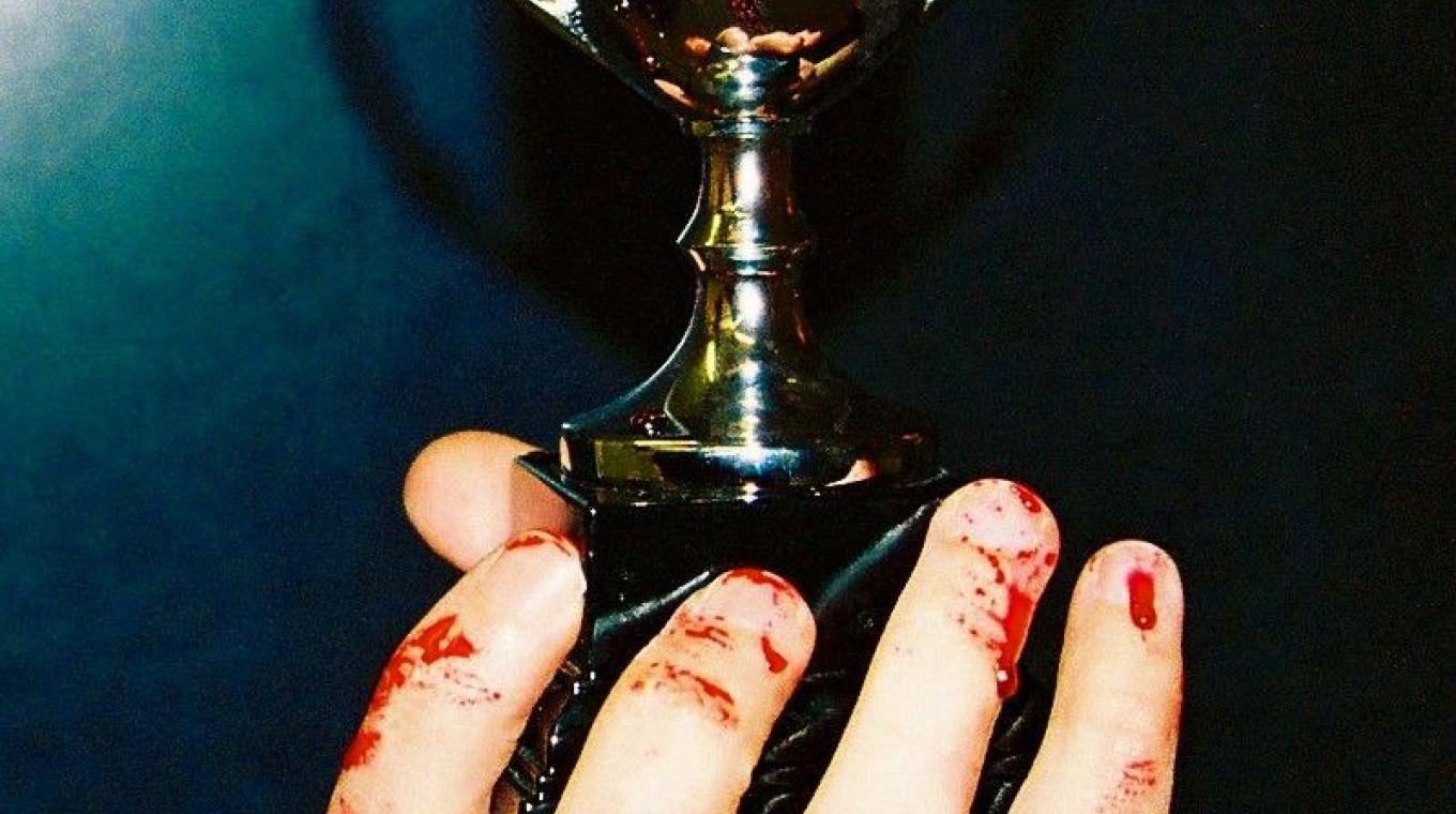 A theatrical image of a bloody hand holding a trophy covered in blood