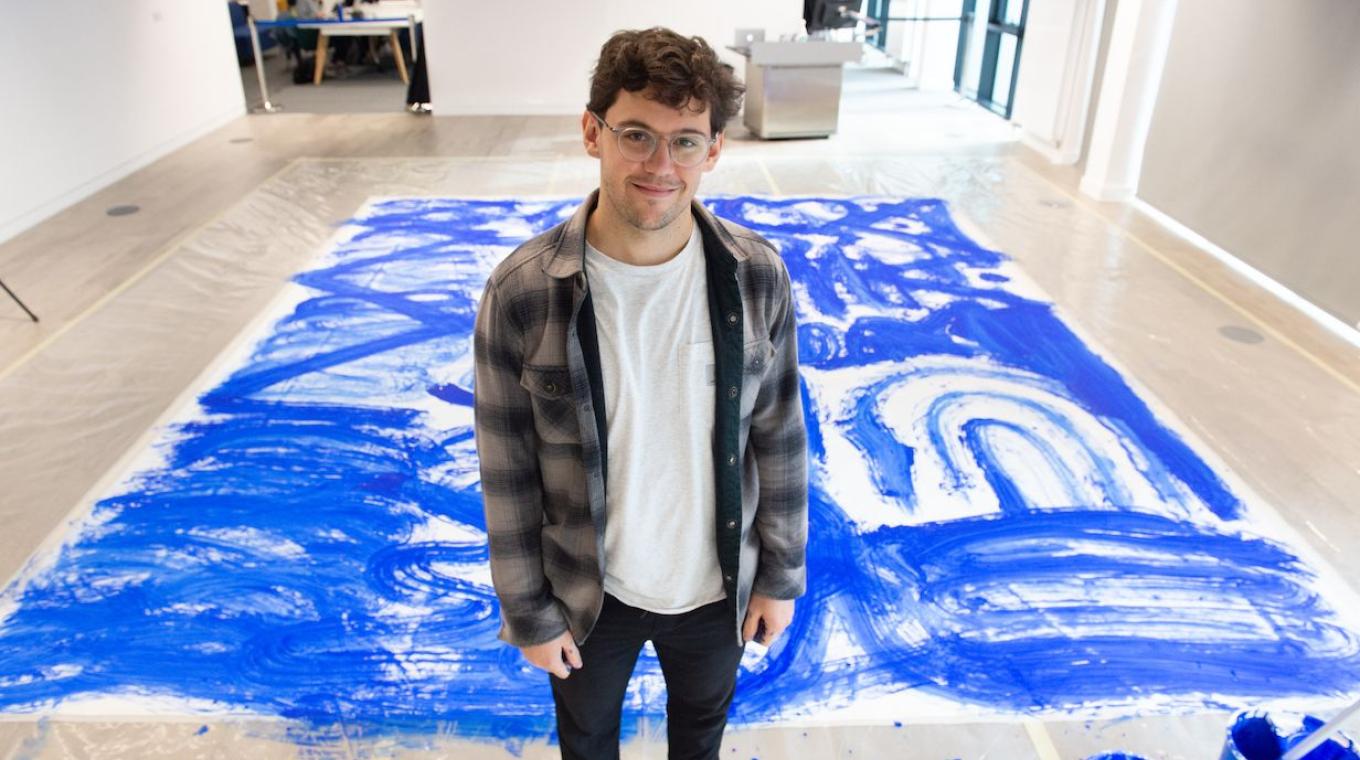 The white male artist José Garcia Oliva wearing circular glasses standing in front of the completed blue artwork on the floor