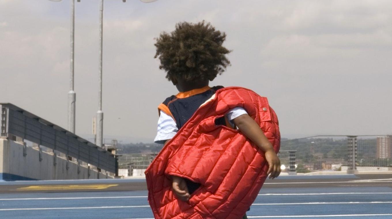 A toddler stood taking off his gilet