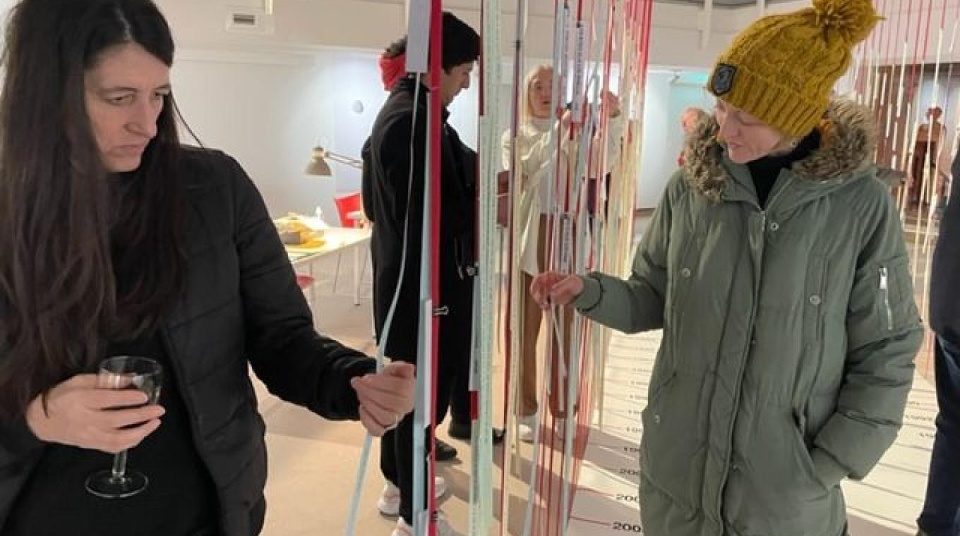 Two women focused on reading thin strips of paper which are hanging from above