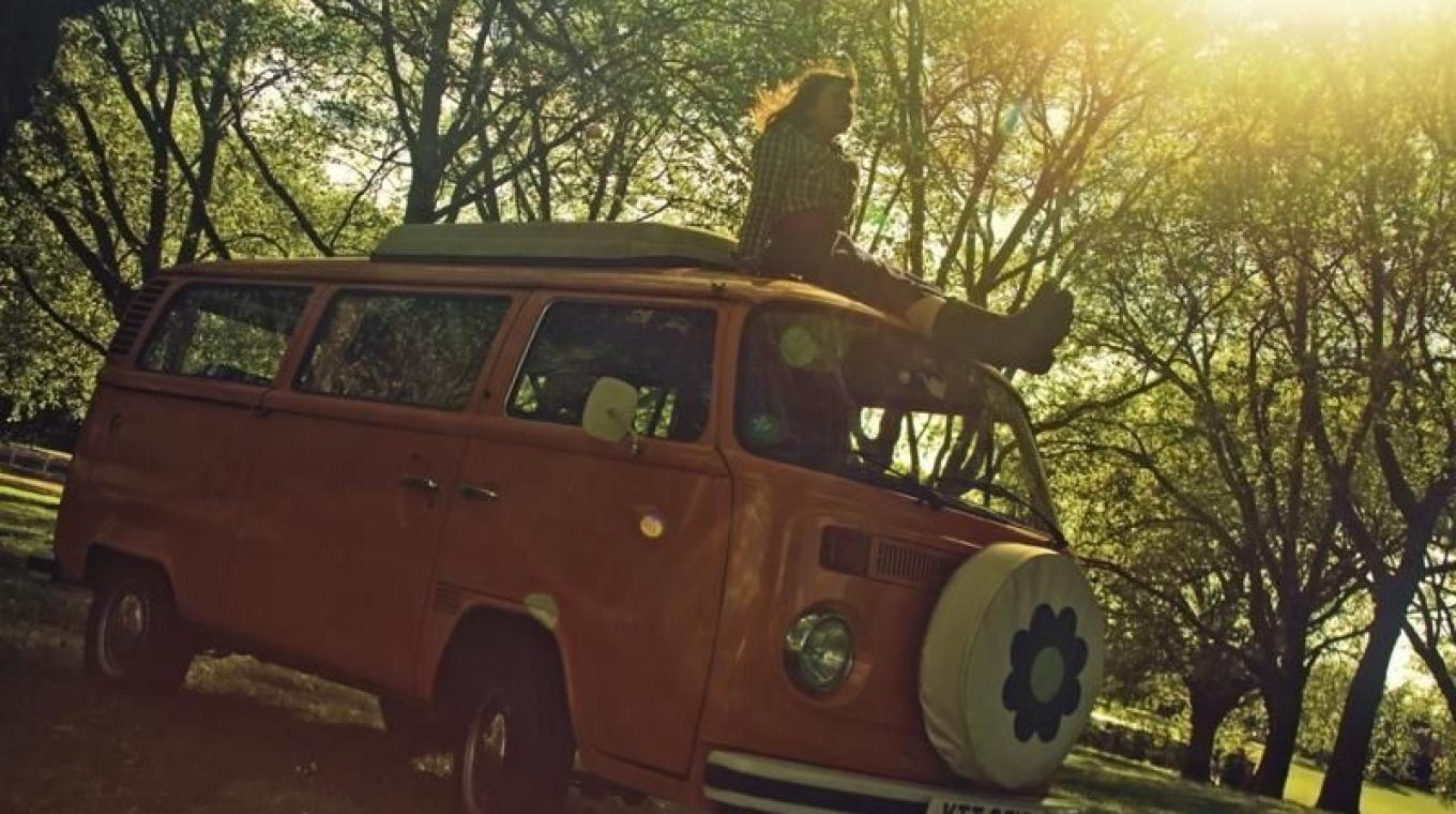 Performer sat on top of a static VW camper van in the sunshine.