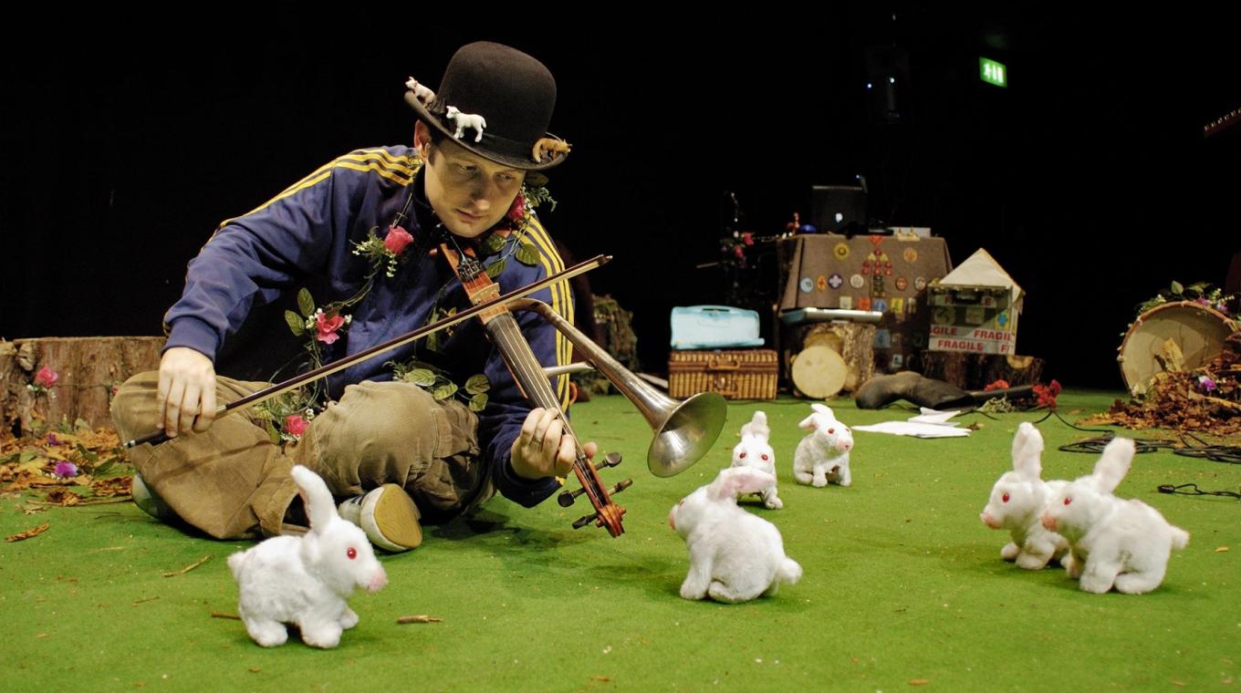 Production Photo. Performer playing violin to stuffed bunnies