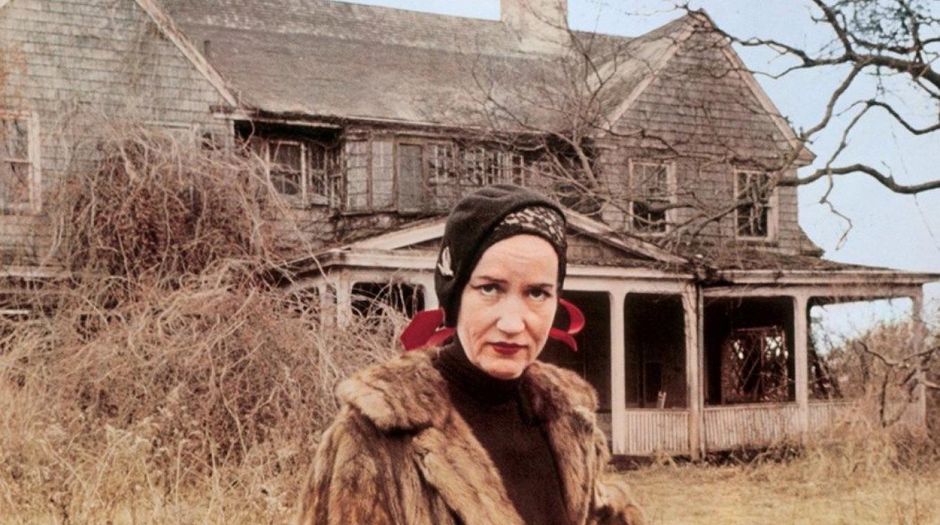 A woman stood in front of a semi-derelict house