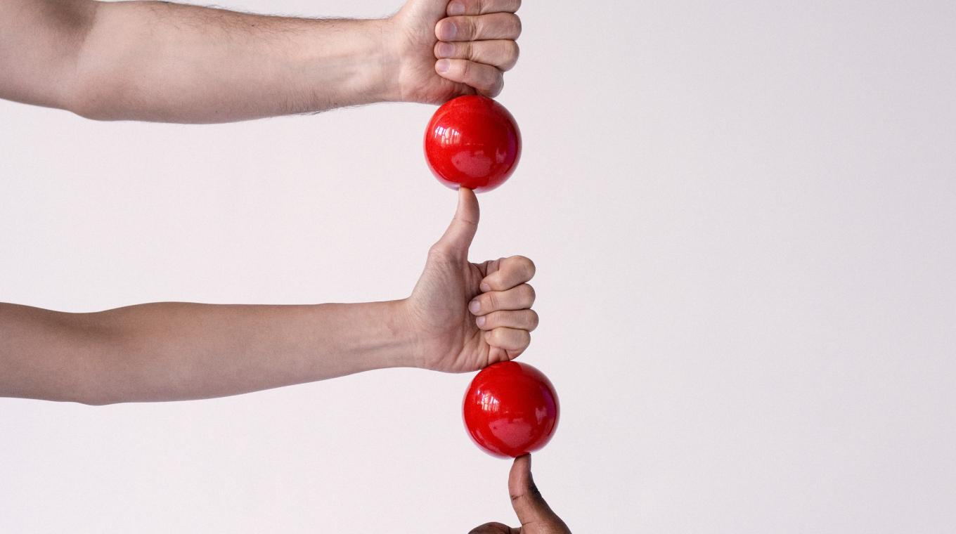 Five hands with their thumbs up in a vertical line with balls balanced on top of each thumb