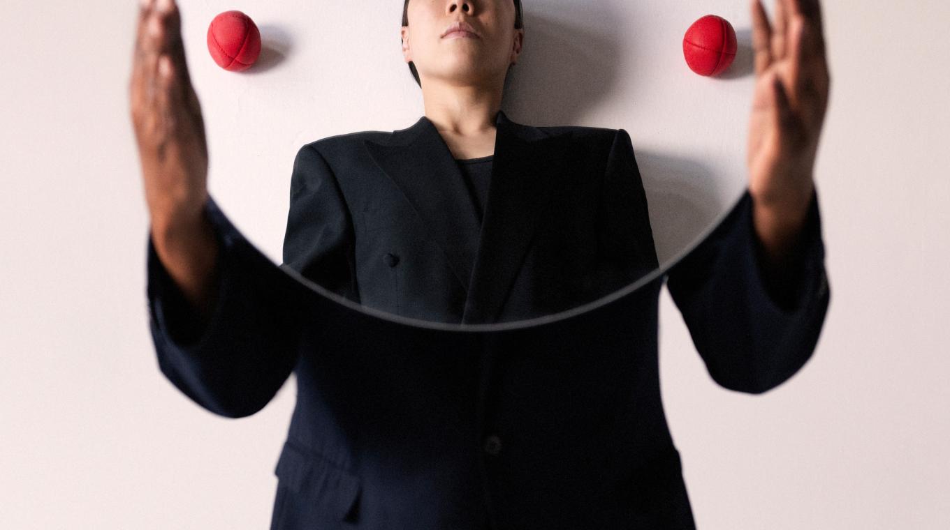 Someone holding a circular mirror with a face and juggling balls reflected in it