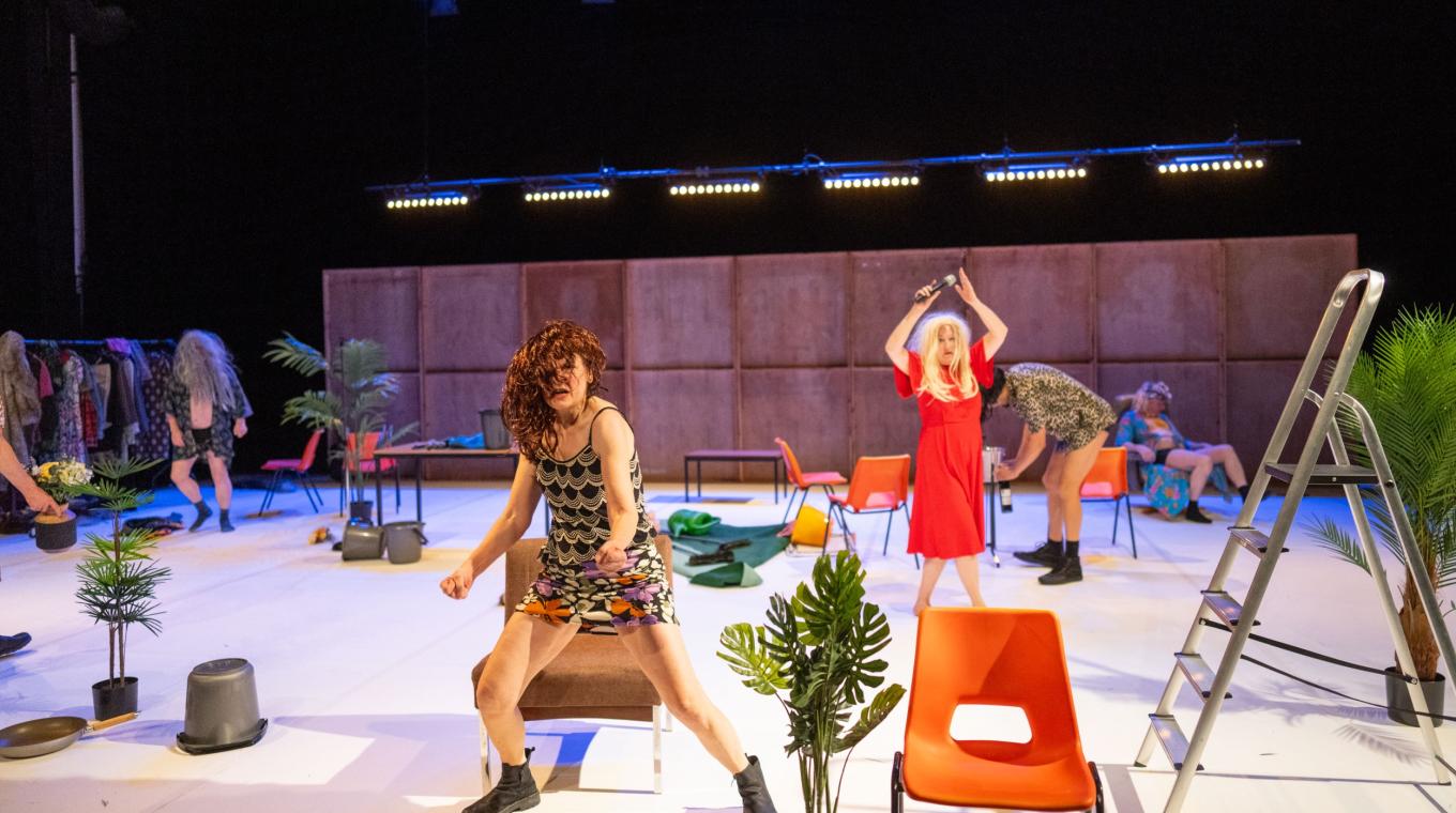 Two people in dresses and wigs on stage with lots of props