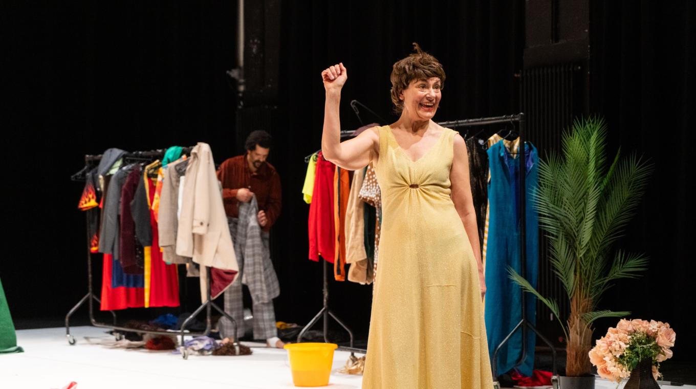 A woman in a dress and wig with clothes rails behind