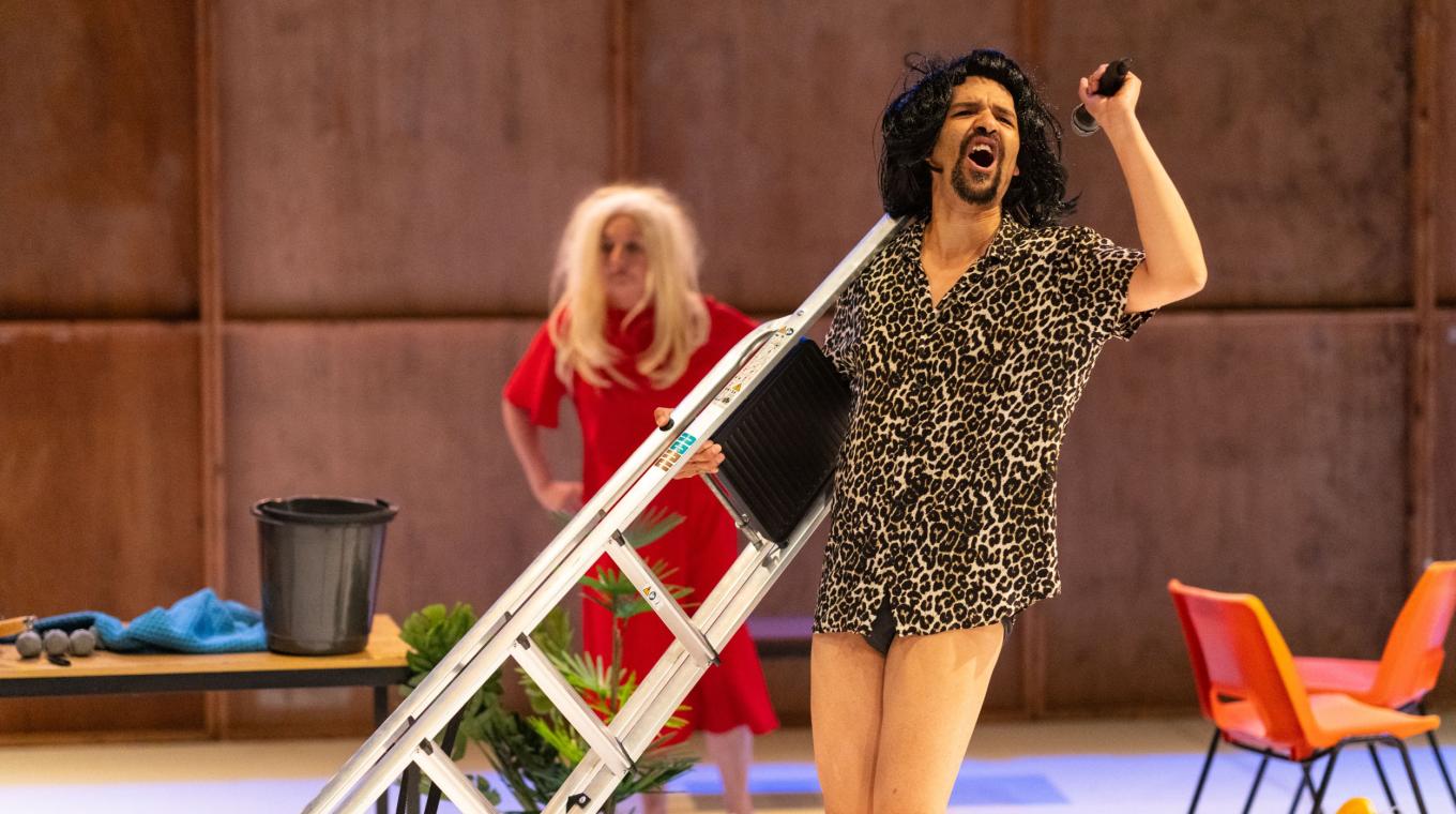 A man in a wig carrying a ladder with a woman in a wig behind