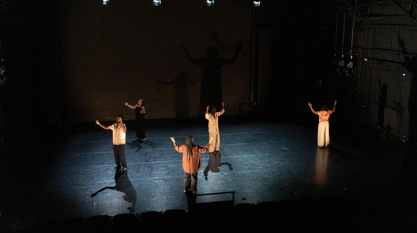 five dancers with their arms raised to the sky