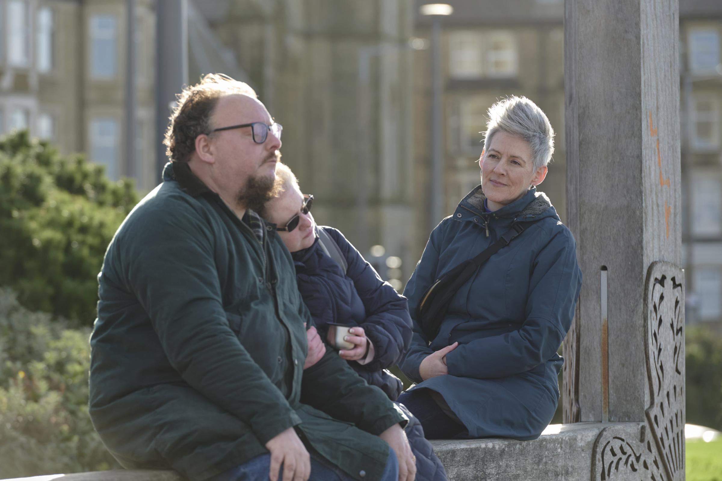 A woman watching and listening to a couple sitting on a bench
