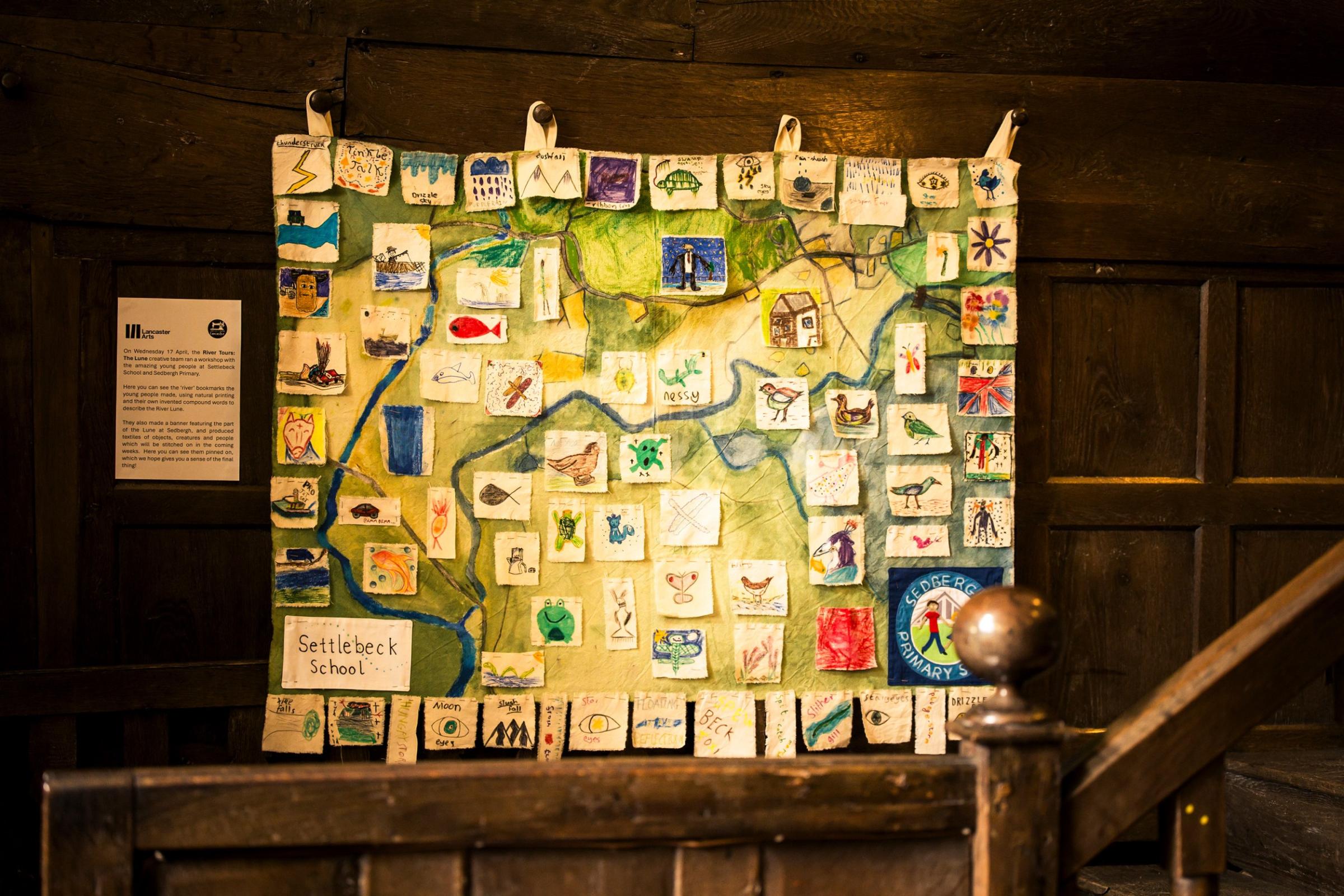 A textile banner of a river with children's drawings pinned on it