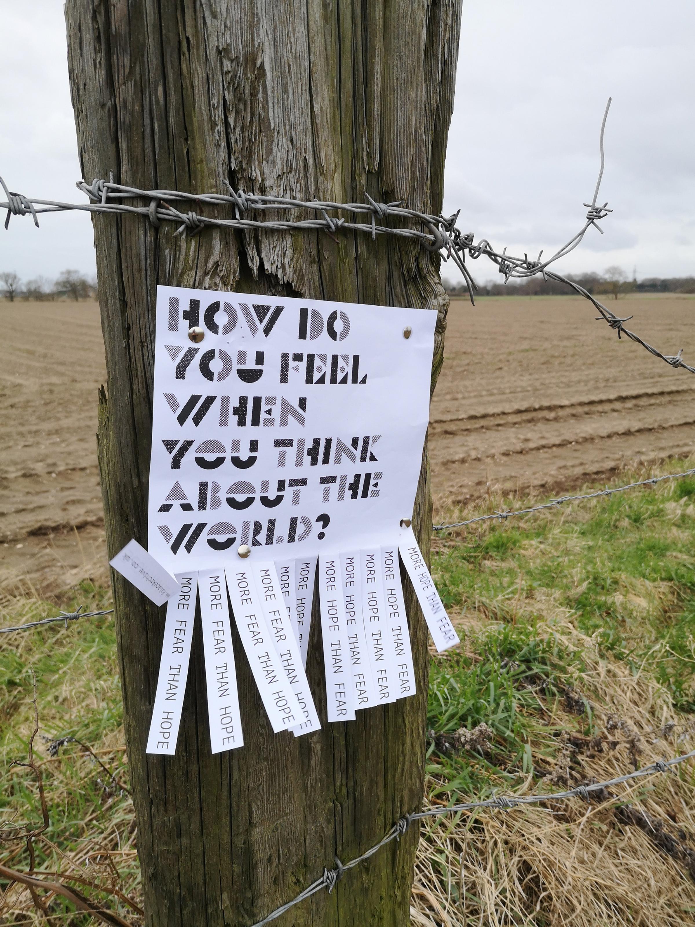 A piece of paper om a fence post thats says "How do you feel when you think about the world"