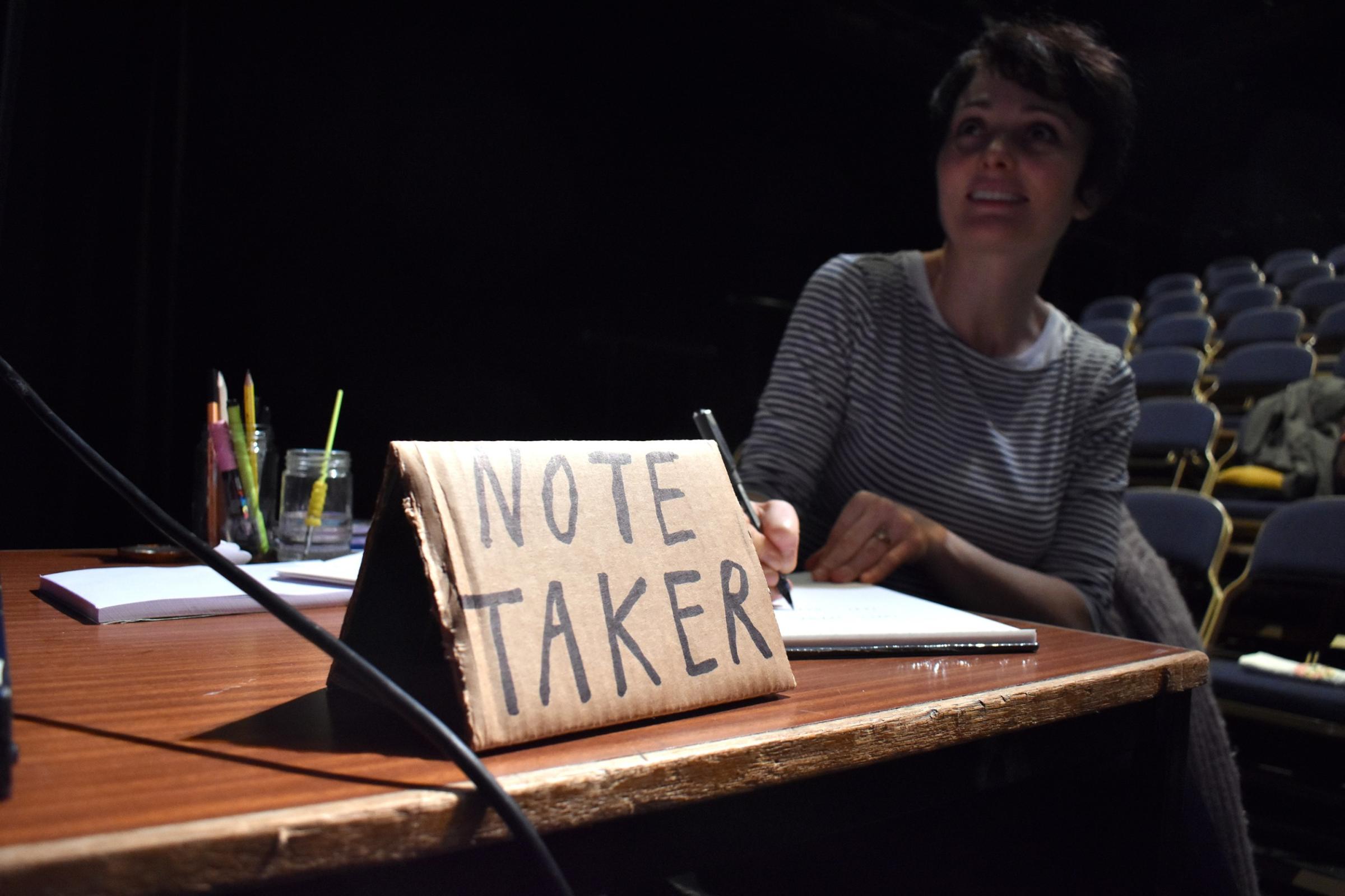 A woman making notes with a sign that reads 'Note Taker'