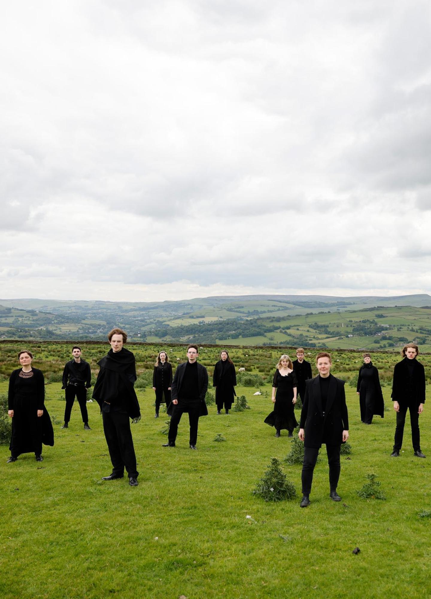 17 people dressed in black standing on a moor with hills behind