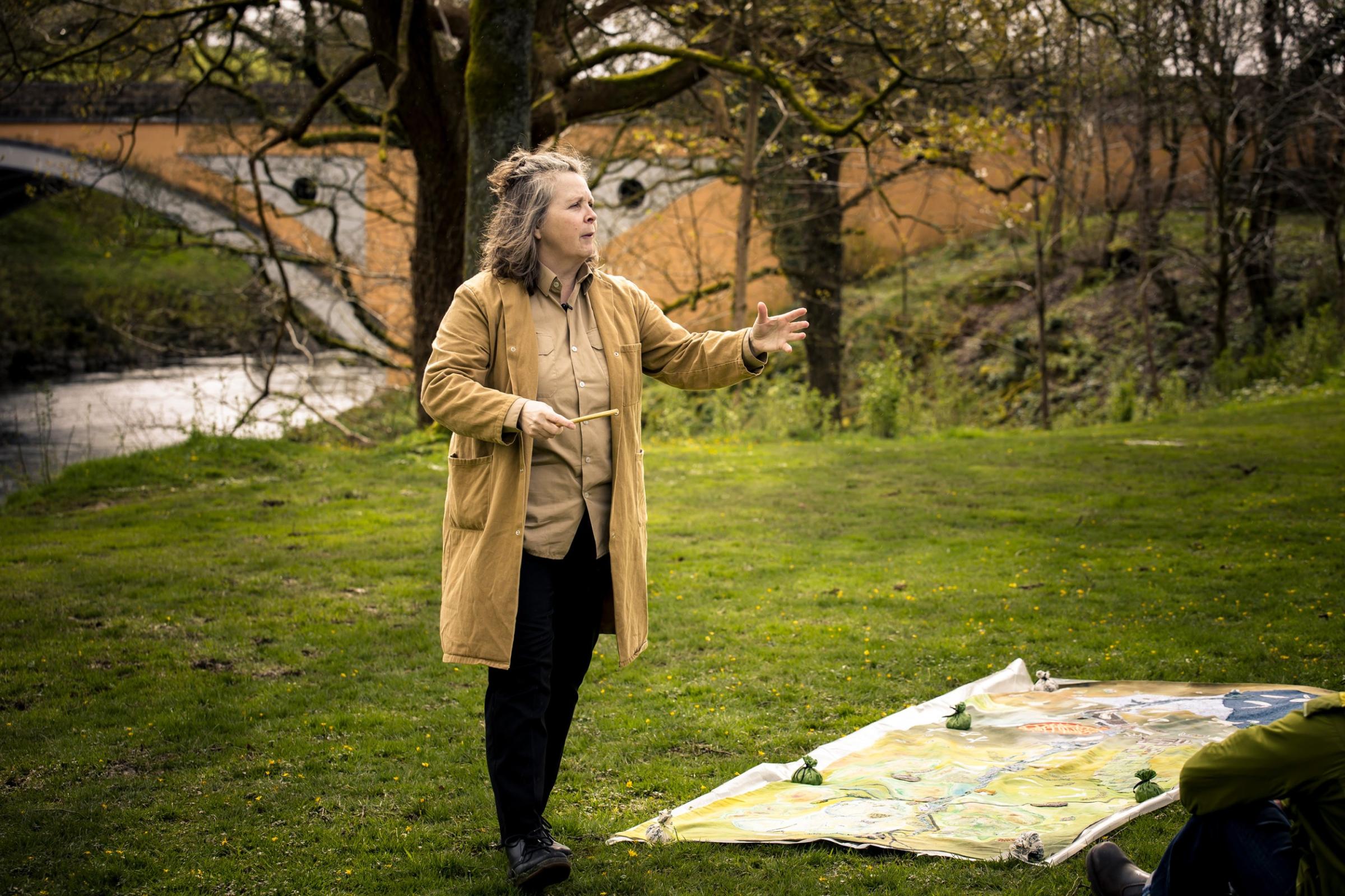 A woman performing by a river with a textile on the ground