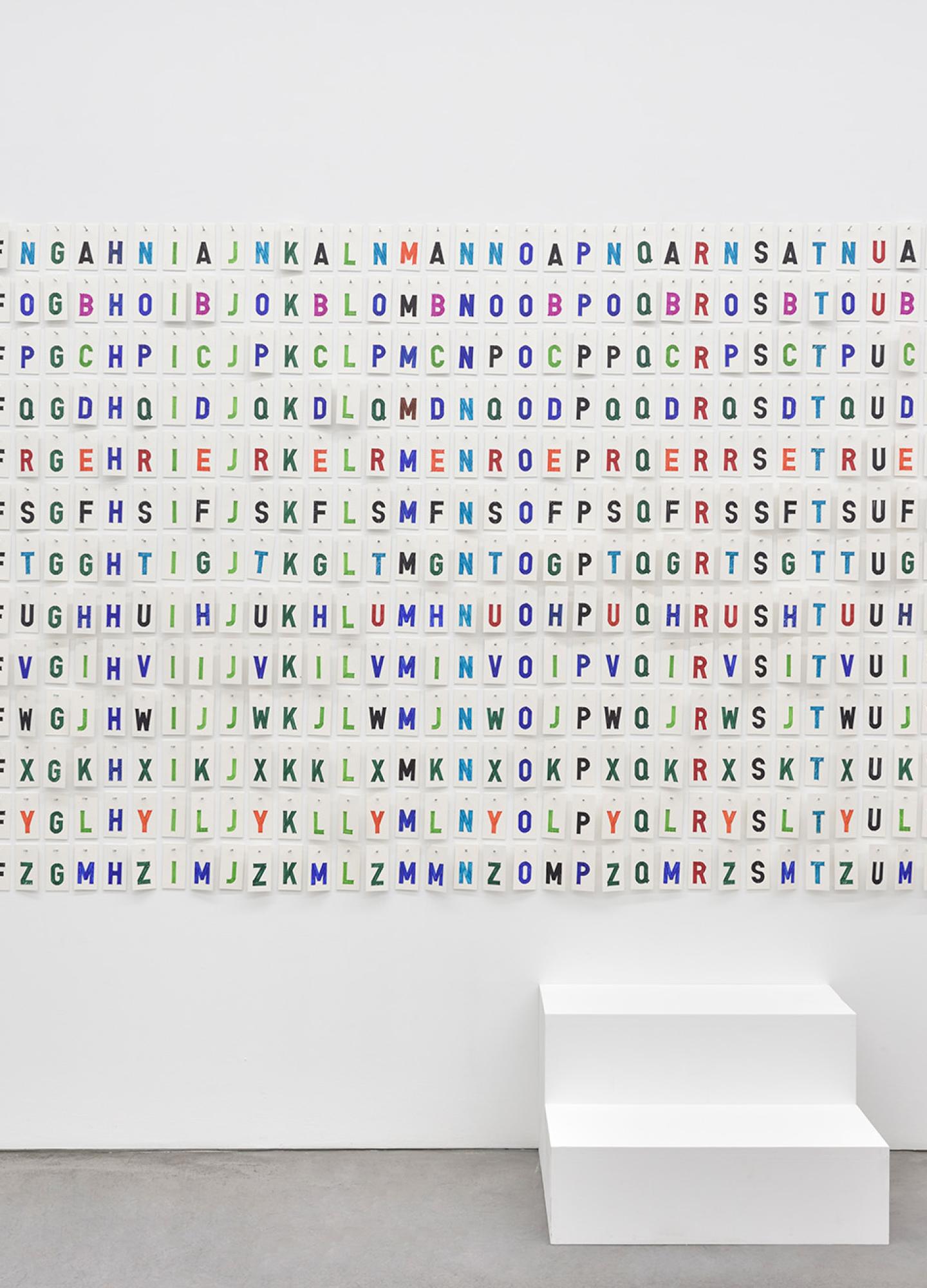 An artwork of hundreds of different coloured letters on a white wall with a white step beneath it