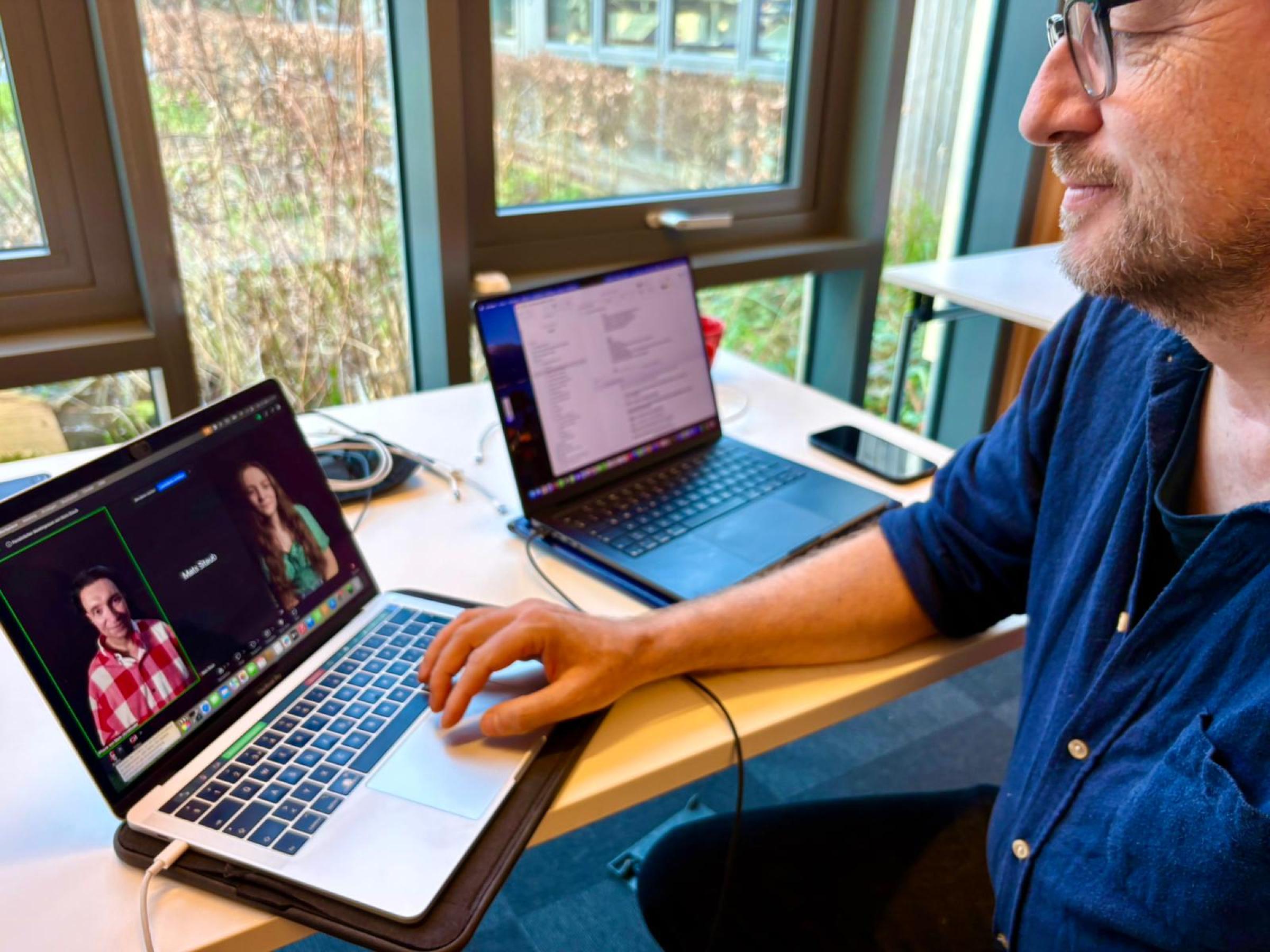 A man using a laptop which shows two other people on the screen