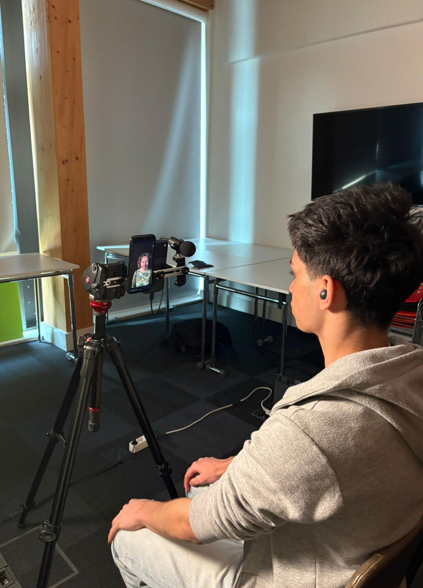 A young person sitting down looking into a camera with a microphone attached