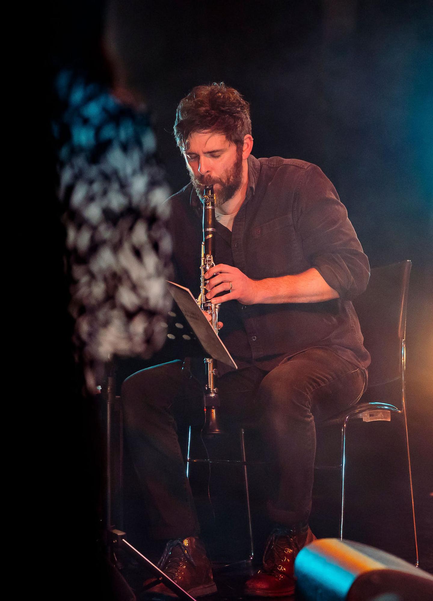 A man playing a clarinet on stage with lights and music stands