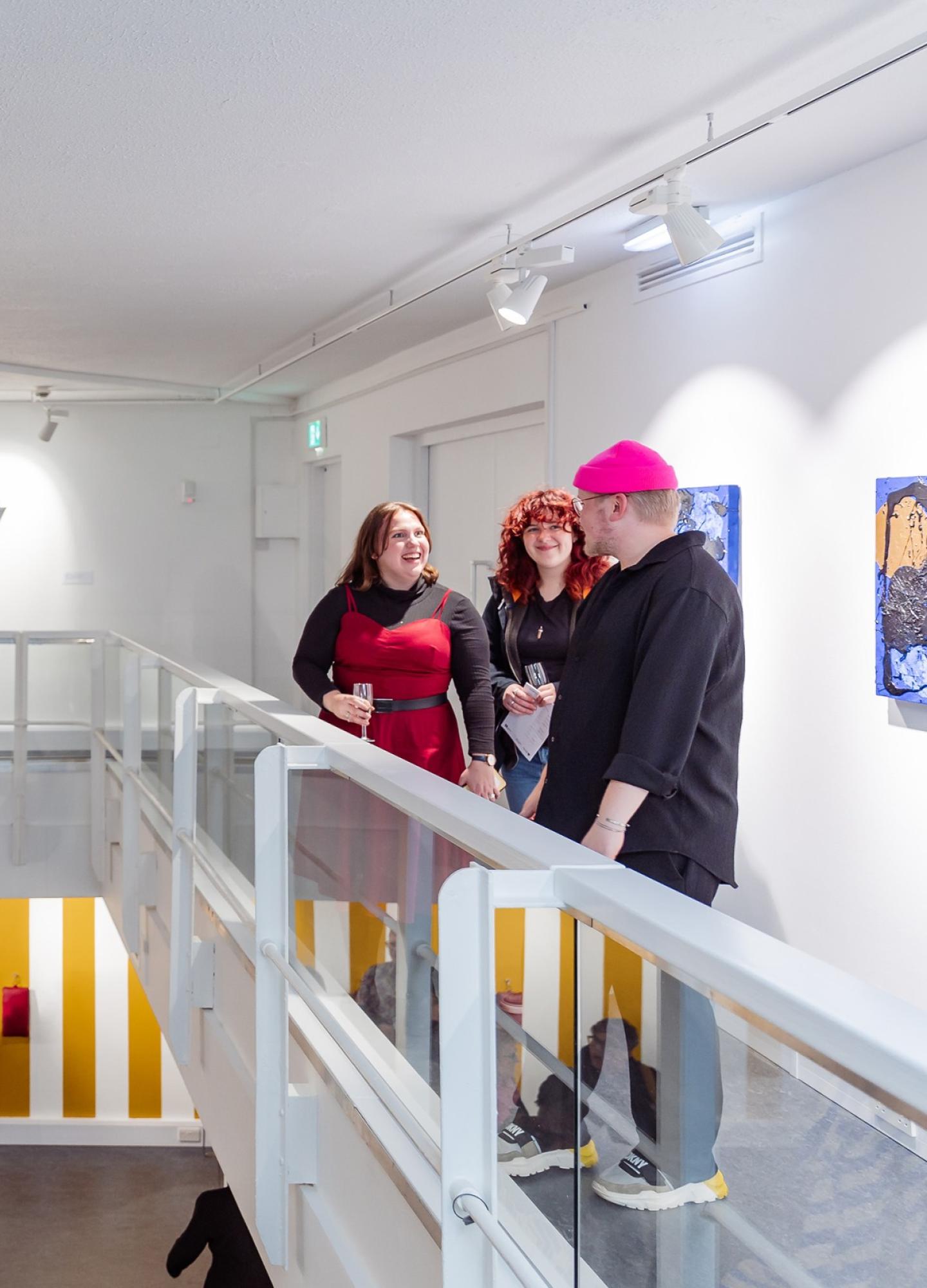 People standing on a balcony in an art gallery with others on the floor below