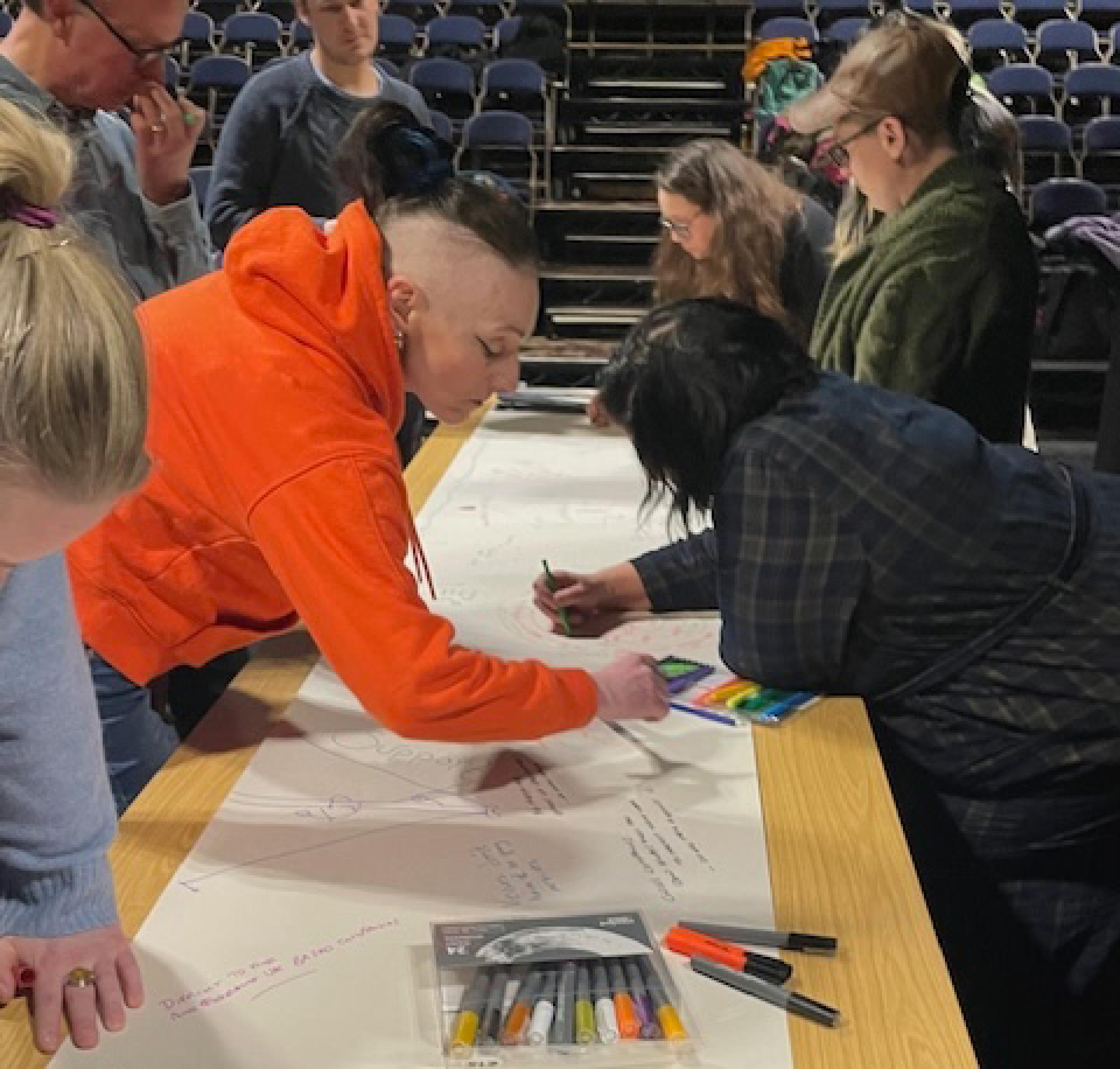 A group of people writing on a long piece of paper across a table
