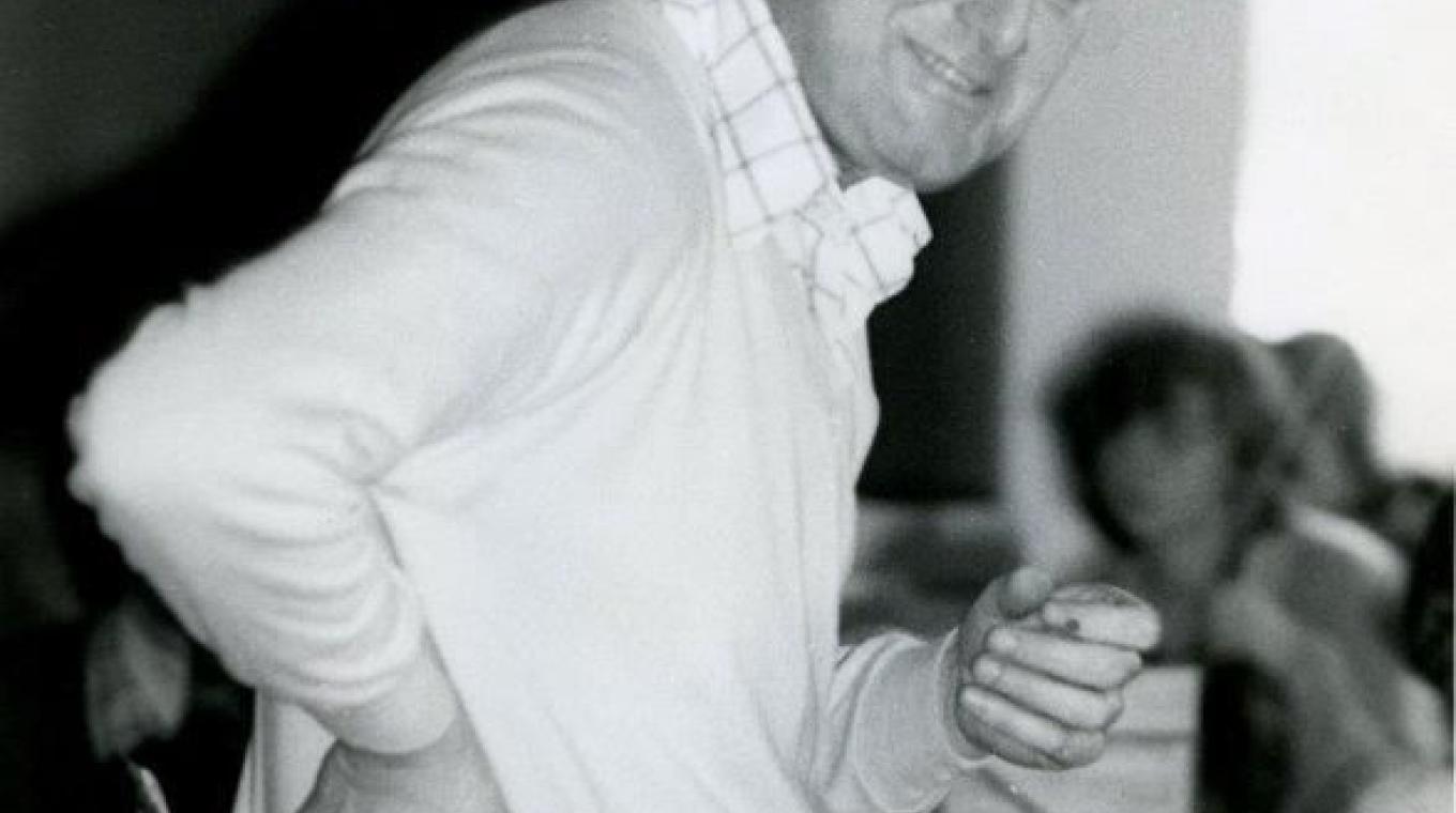 Black and white photo of a white male looking at the camera, stood in front of music stands