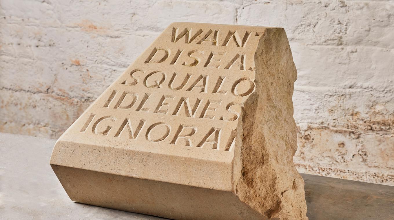 A large sand coloured stone sculpture broken in half with the words "Want Disease Squalor Idleness Ignorance" have visible engraved on it