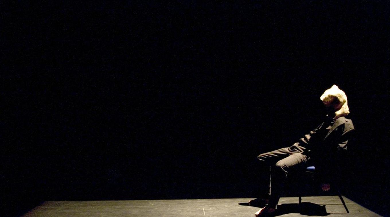 Stage Photo of a man sat n a chair with a bag over his head.