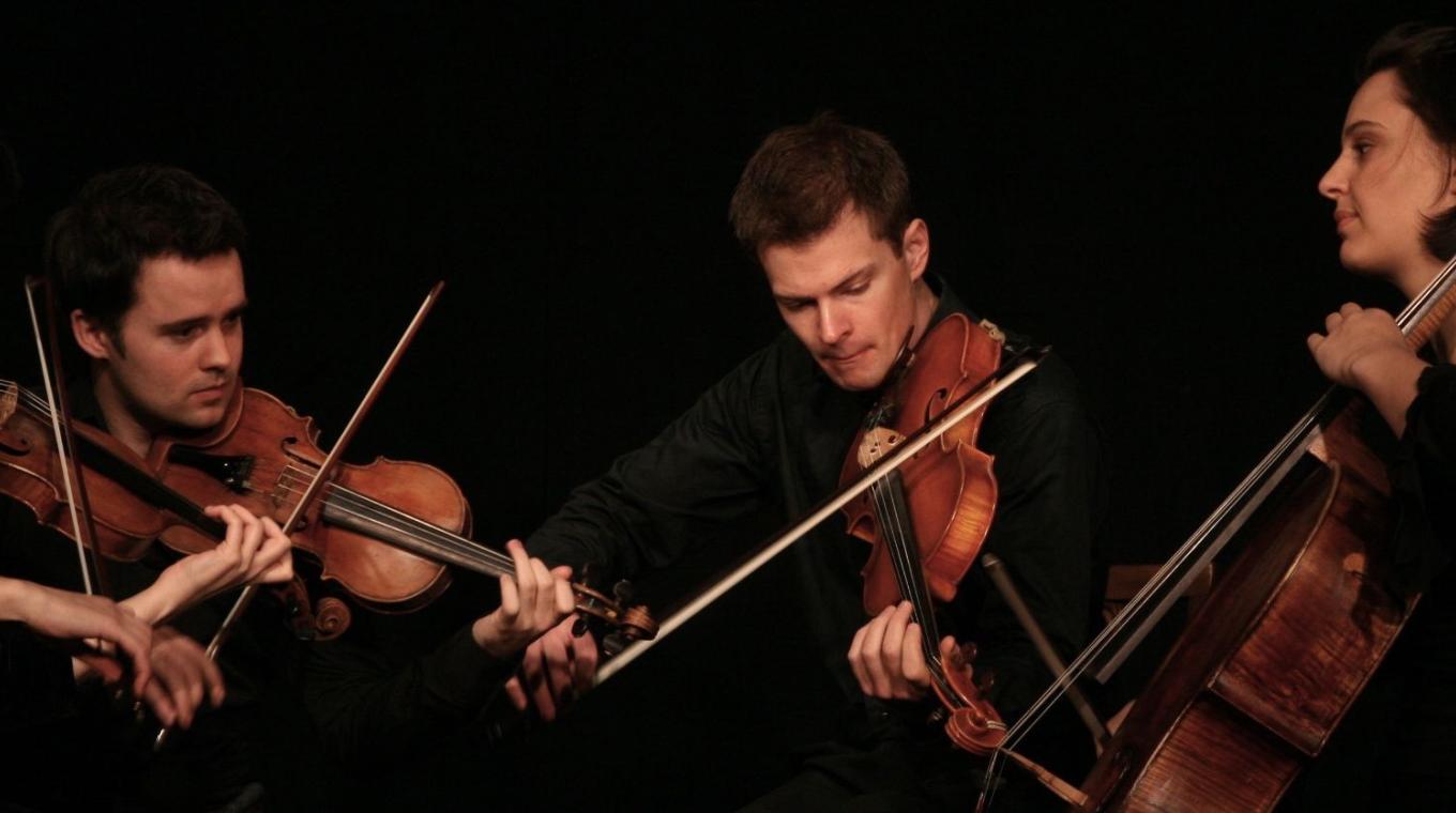 3 violinists and a cellist on stage performing.