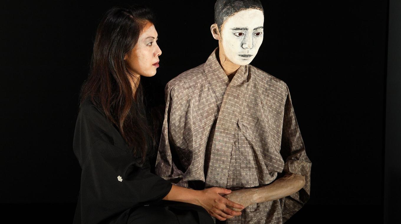 Two performers on stage, one with a painted white mask on his face.