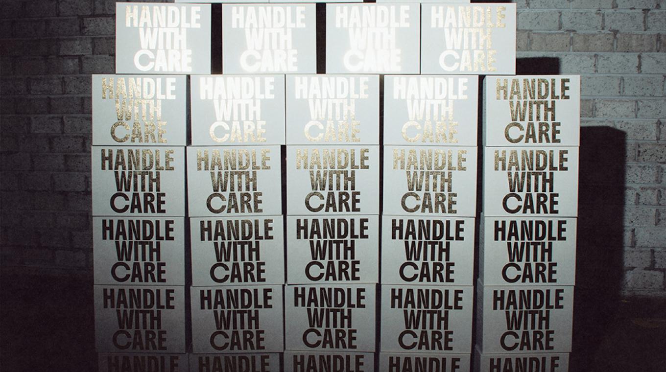 A large stack of identical white boxes with the words "handle with care" written on each