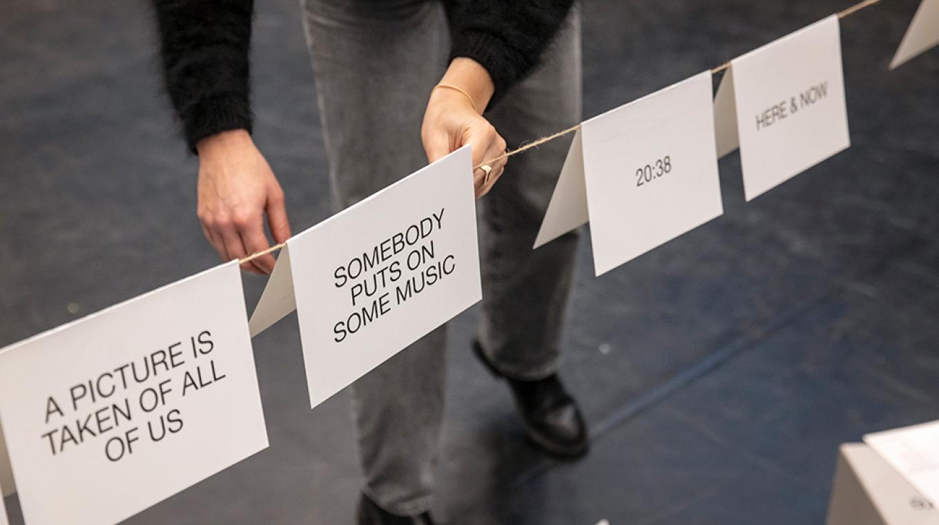 A person putting a card that says 'Somebody puts on some music" on a piece of string