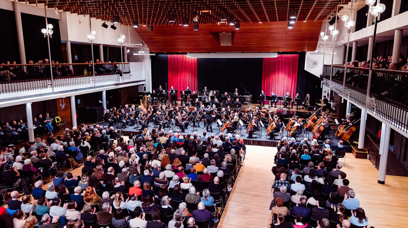 A full audience in a concert hall with an orchestra on stage