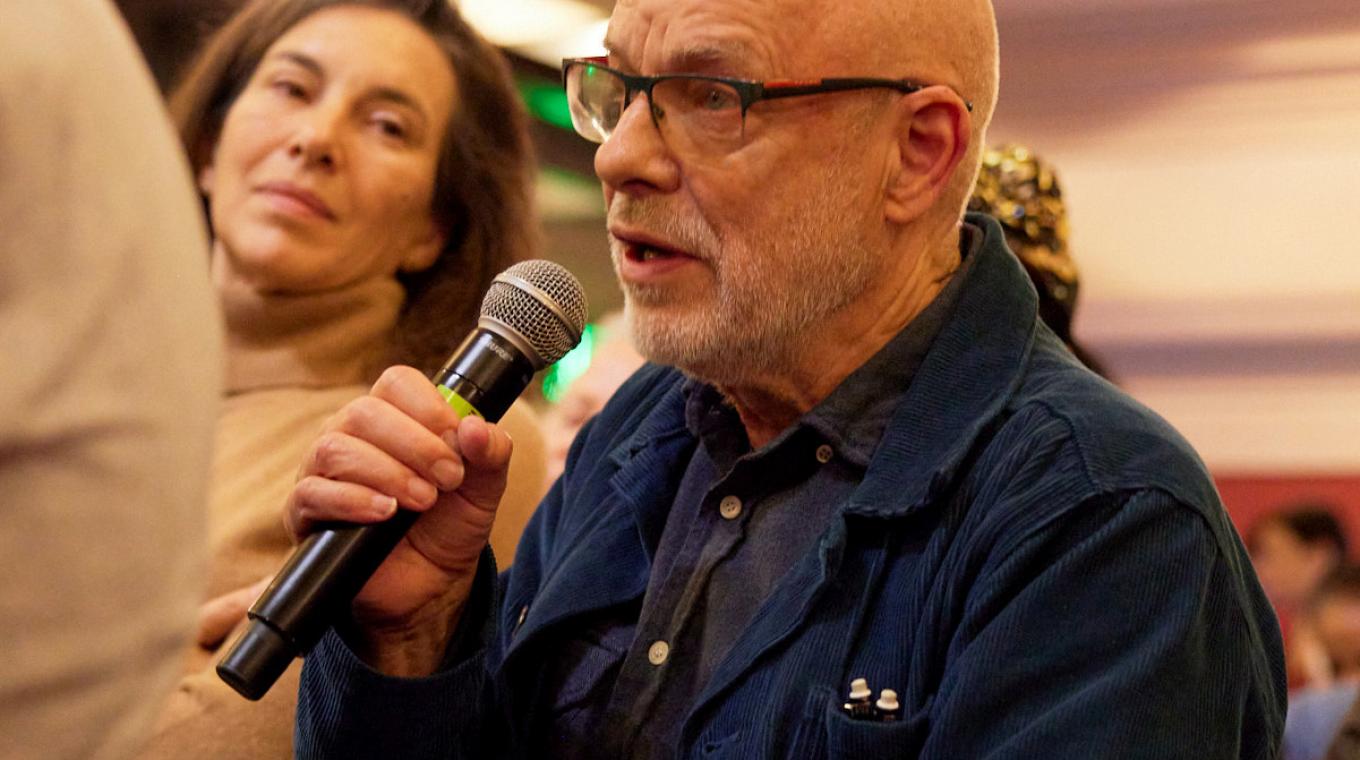 Brian Eno, a bald man, speaking into a microphone in the audience