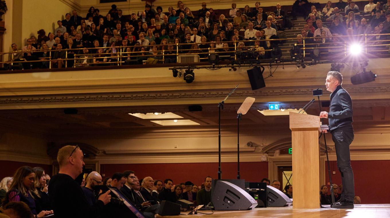 Chris Packham on a podium speaking to a hall full of people