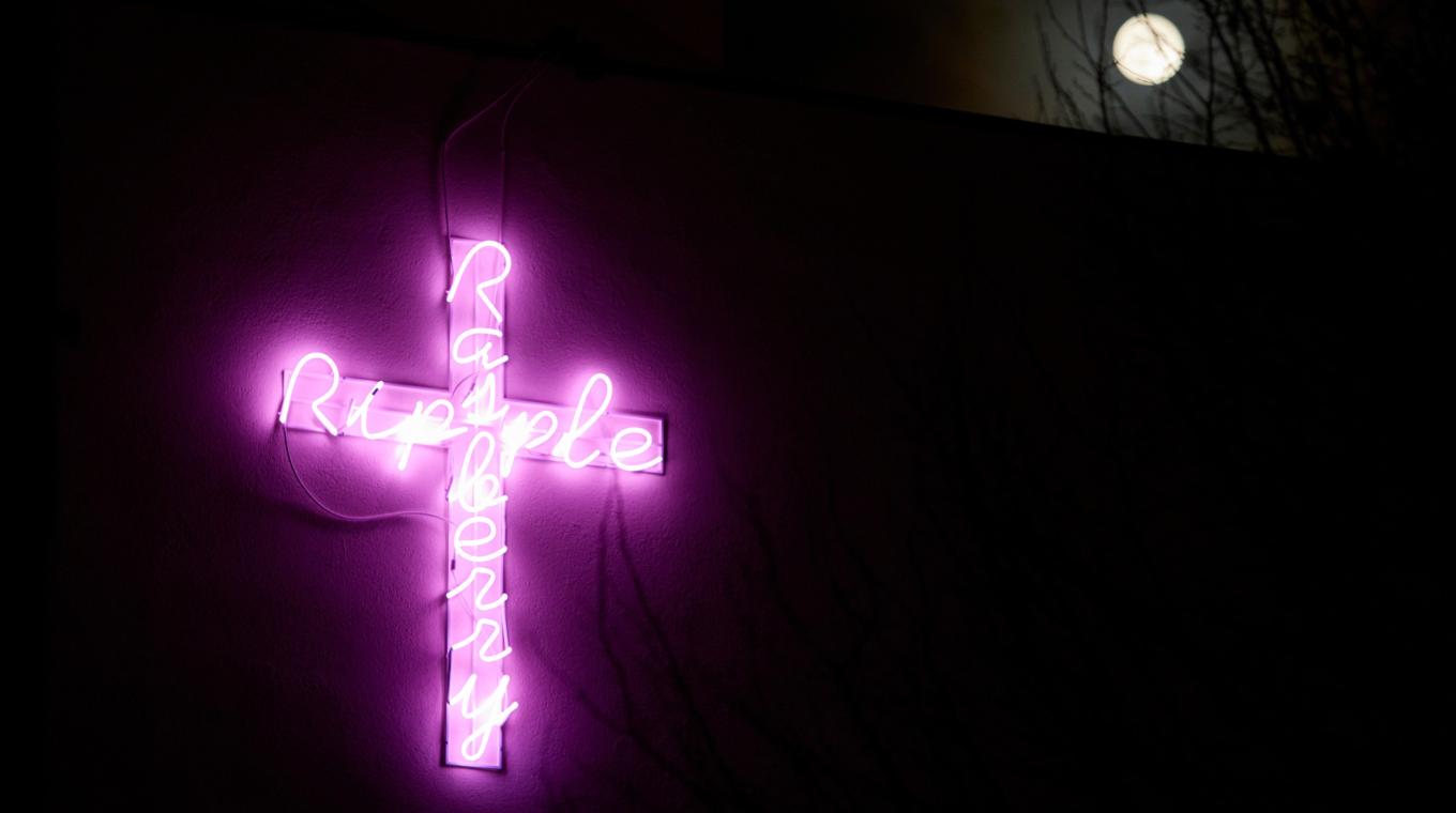 A pink neon sign of the words "Rasberry Ripple" on the side of a building at night with the moon in the background